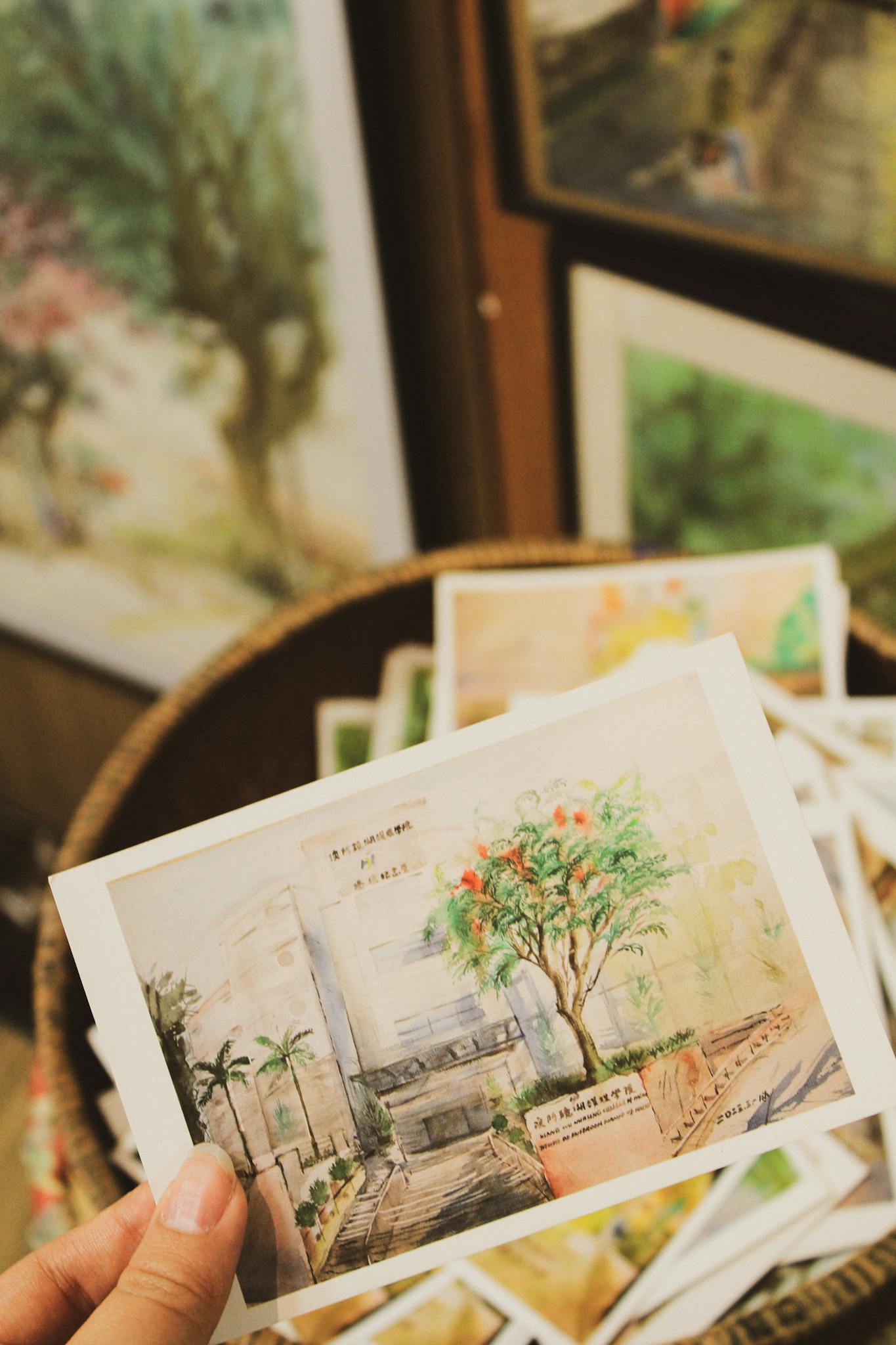 A hand holding a watercolor postcard depicting a scenic view in Macao, ideal for travel promotion.