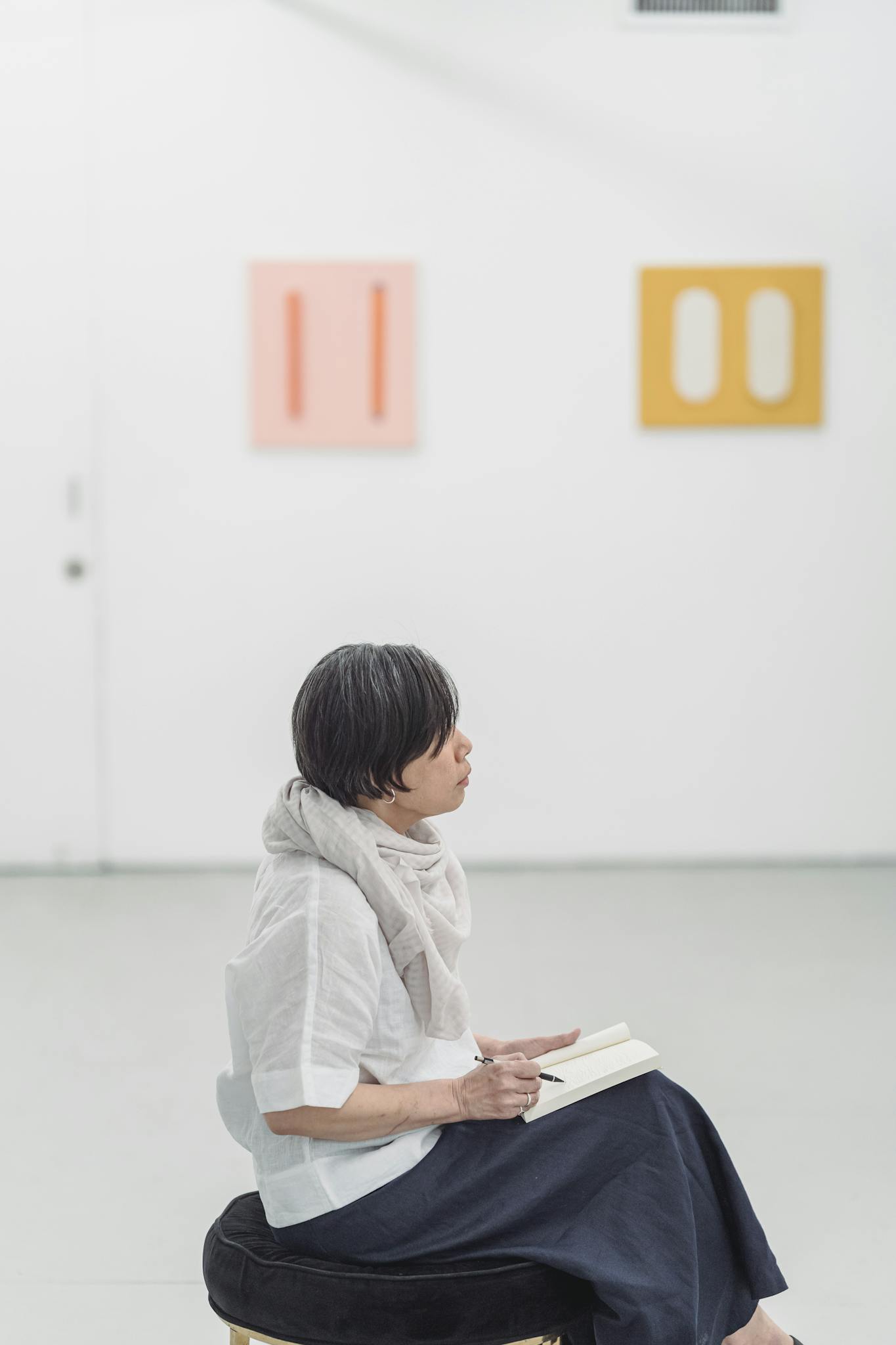 A woman seated in a gallery, immersed in thought with a sketchpad.